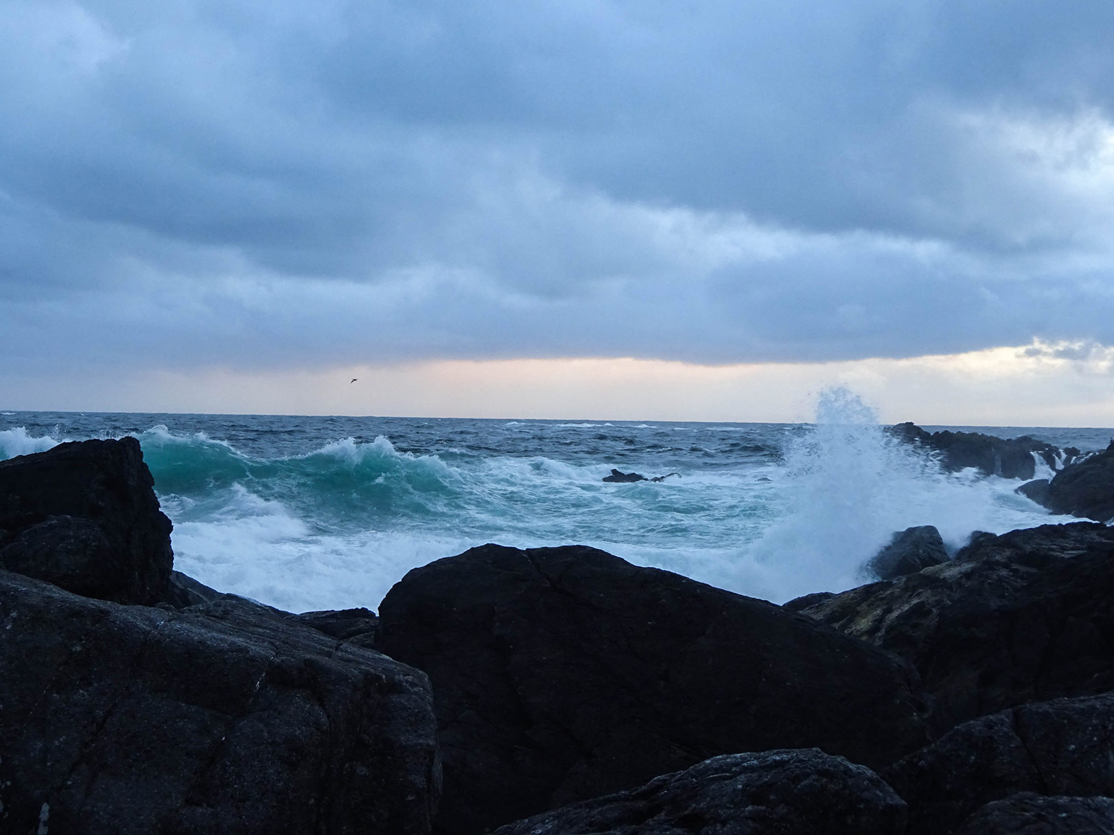 Waves crashing against a rocky shore in a stormy sunset.